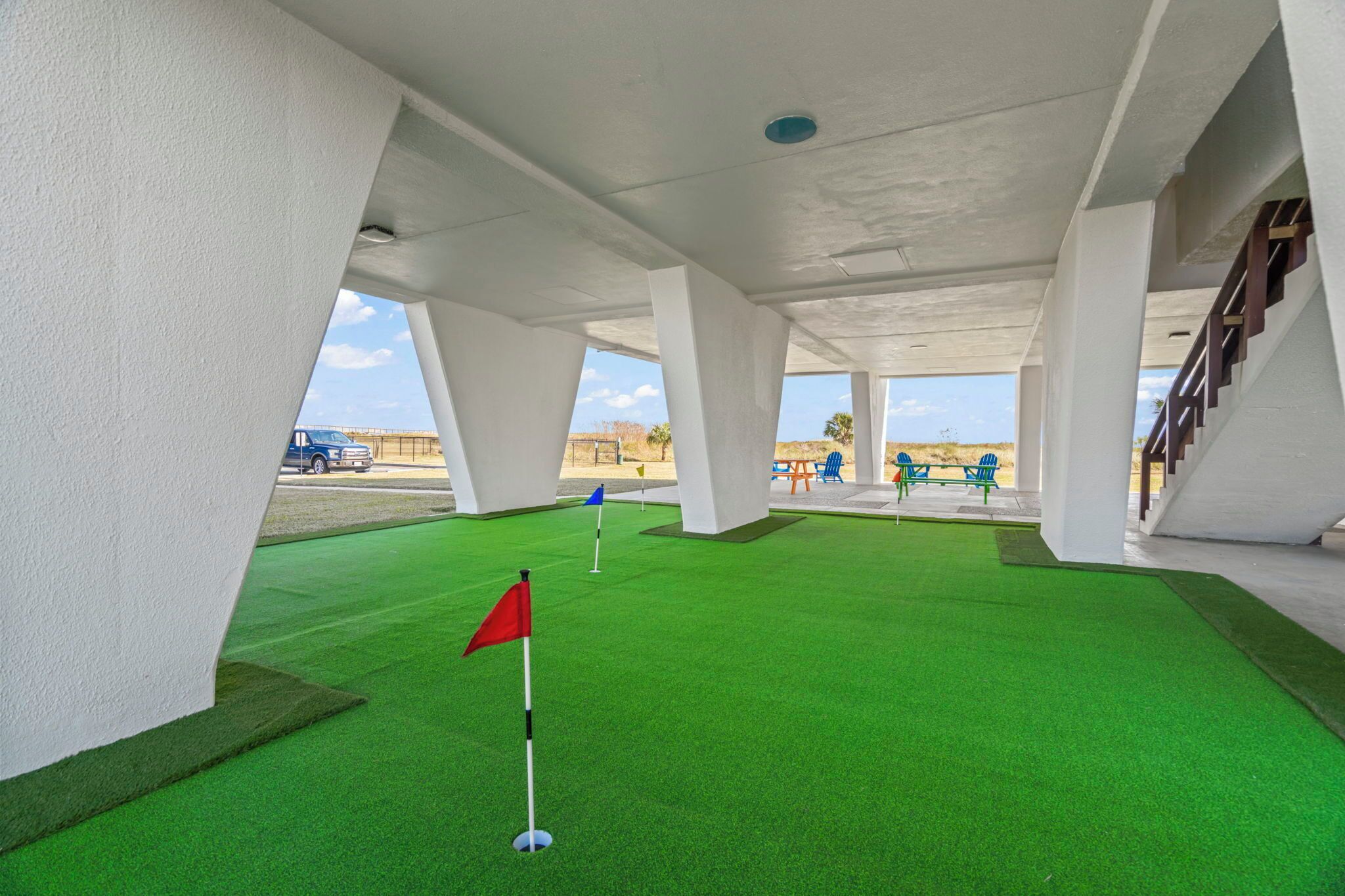 Un espace d’entraînement de golf intérieur doté d’un revêtement de sol synthétique, d’un drapeau rouge et d’un drapeau bleu.