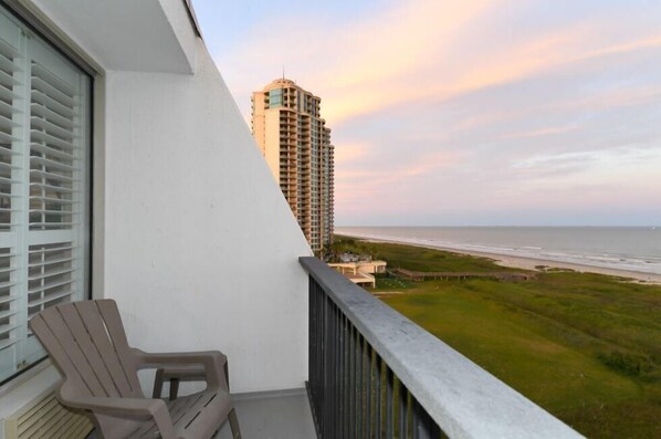 A balcony with a view of the beach and a tall building in the background.