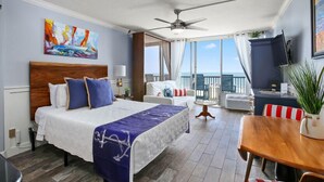 A hotel room with a large bed, a ceiling fan, a balcony with a view, and a dining area.