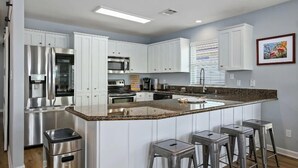 Een moderne keuken met witte kasten, roestvrijstalen apparatuur, een granieten aanrecht en barstoelen.