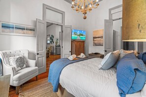Ein Schlafzimmer mit einem großen Bett, einem weißen Sessel, einem Fernseher und einer Kristallleuchter.
