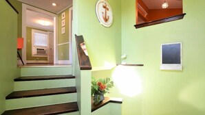 Eine Treppe mit Holzstufen führt zu einer Zwischenebene mit einer grünen Wand, einem gerahmten Bild und einem kleinen Regal mit einer Vogelstatue.