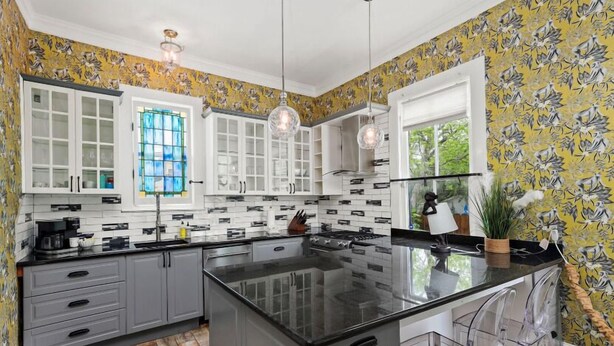 Une cuisine moderne avec des meubles gris, un îlot central noir et une grande fenêtre ornée de vitraux.