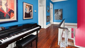 Une pièce avec un piano, des œuvres d’art encadrées accrochées aux murs et un escalier dont l’un des murs est peint en rouge.