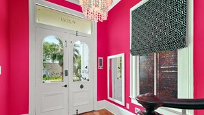 Un couloir avec un mur rose vif, une porte blanche dotée de panneaux de verre et un lambrequin à motifs noir et blanc.