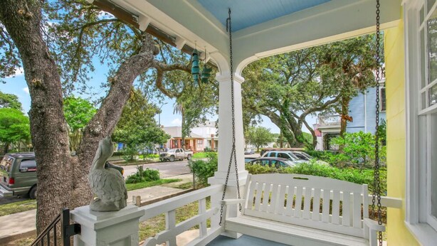 A porch with a white swing, a stone bird sculpture, and a view of a street with parked cars and houses. - Welcome to "The Sunrise Inn!" (Galveston)