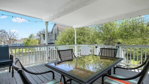 A covered outdoor patio with a glass-top table and chairs, surrounded by a white railing.