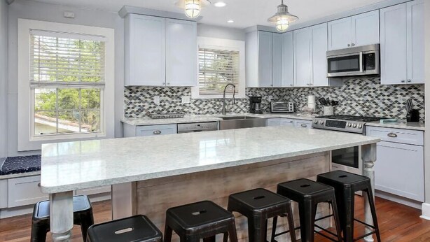 A modern kitchen with a large island, bar stools, and a microwave.