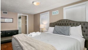 A hotel room with a large bed, a bedside table with a lamp, a wardrobe, and a window with blinds.