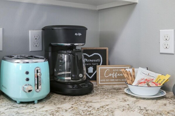 Una cocina con cafetera, tostadora y un tazón de sobres de café.