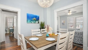 A dining area with a wooden table set for four, white chairs, a chandelier, and a painting of an underwater scene.