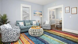 A living room with a sofa, armchair, and coffee table, a ceiling fan, and a colorful striped rug.
