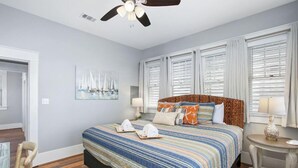 A bedroom with a large bed, a ceiling fan, and a painting of sailboats on the wall.