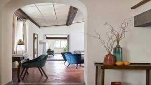Un pasillo amplio con techo alto, suelo de madera y vista a otra habitación. Hay una mesa con un florero y un libro.