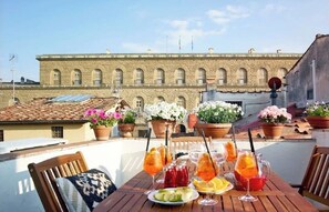Une terrasse sur le toit, avec une table dressée pour le dîner, des plantes en pot et, en arrière-plan, un bâtiment doté de fenêtres en arc de cercle.