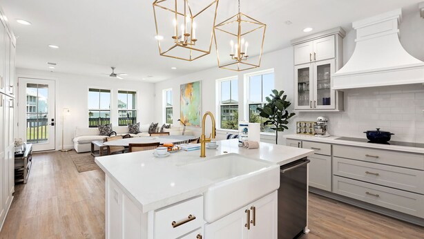 Une cuisine moderne avec des meubles blancs, un grand îlot central doté d’un évier et des luminaires suspendus.