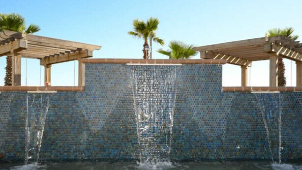 A water feature with a tiled wall and wooden pergolas.