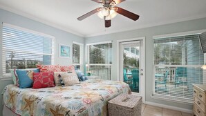 A bedroom with a bed, a ceiling fan, a window with blinds, and a view of the outside.