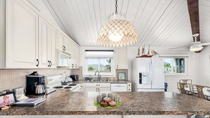 A modern kitchen with white cabinetry, granite countertops, a large island with bar seating, a hanging pendant light, and a view of the outdoors through the windows. - Sea Isle Sailfish! Canal front in popular Sea Isle! Pet Friendly! (Galveston)