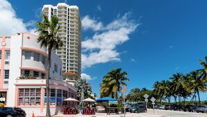 A tall hotel with a curved facade, palm trees, and outdoor seating areas. - Remodeled Beachfront Studio w/ Beach Essentials. Just steps from the beach!  (Miami Beach)