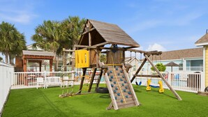 Ein Spielplatz mit einer hölzernen Kletterkonstruktion, einer Rutsche und Schaukeln.