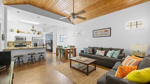 Ein geräumiger Wohnbereich mit Deckenventilator, eine Küche mit modernen Geräten, eine Essecke mit Tisch und Stühlen und eine gemütliche Sitzecke mit Sofa und Kissen.