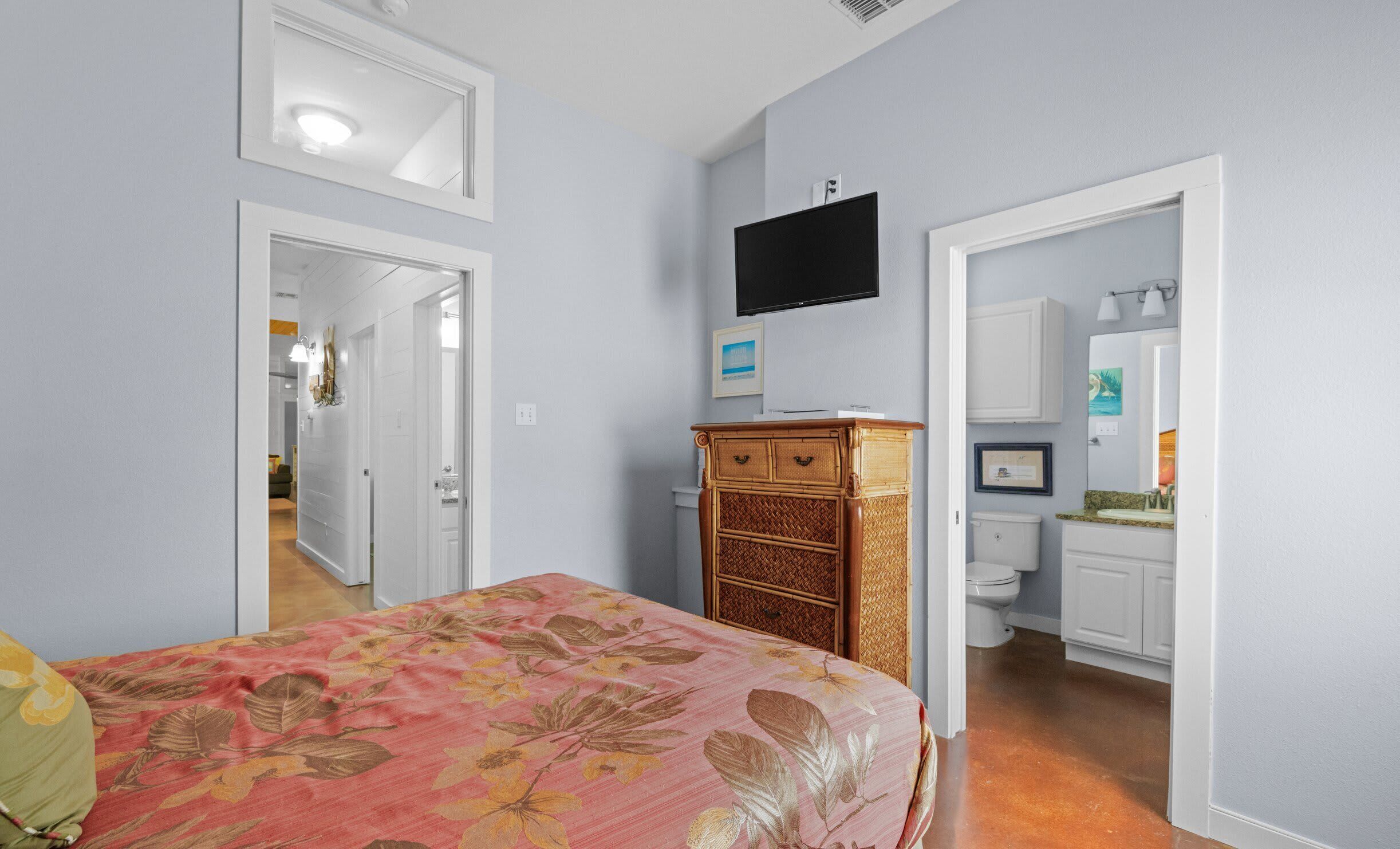 Een slaapkamer met een bed, een kaptafel, een televisie en een zichtbare badkamer door een geopende deur.