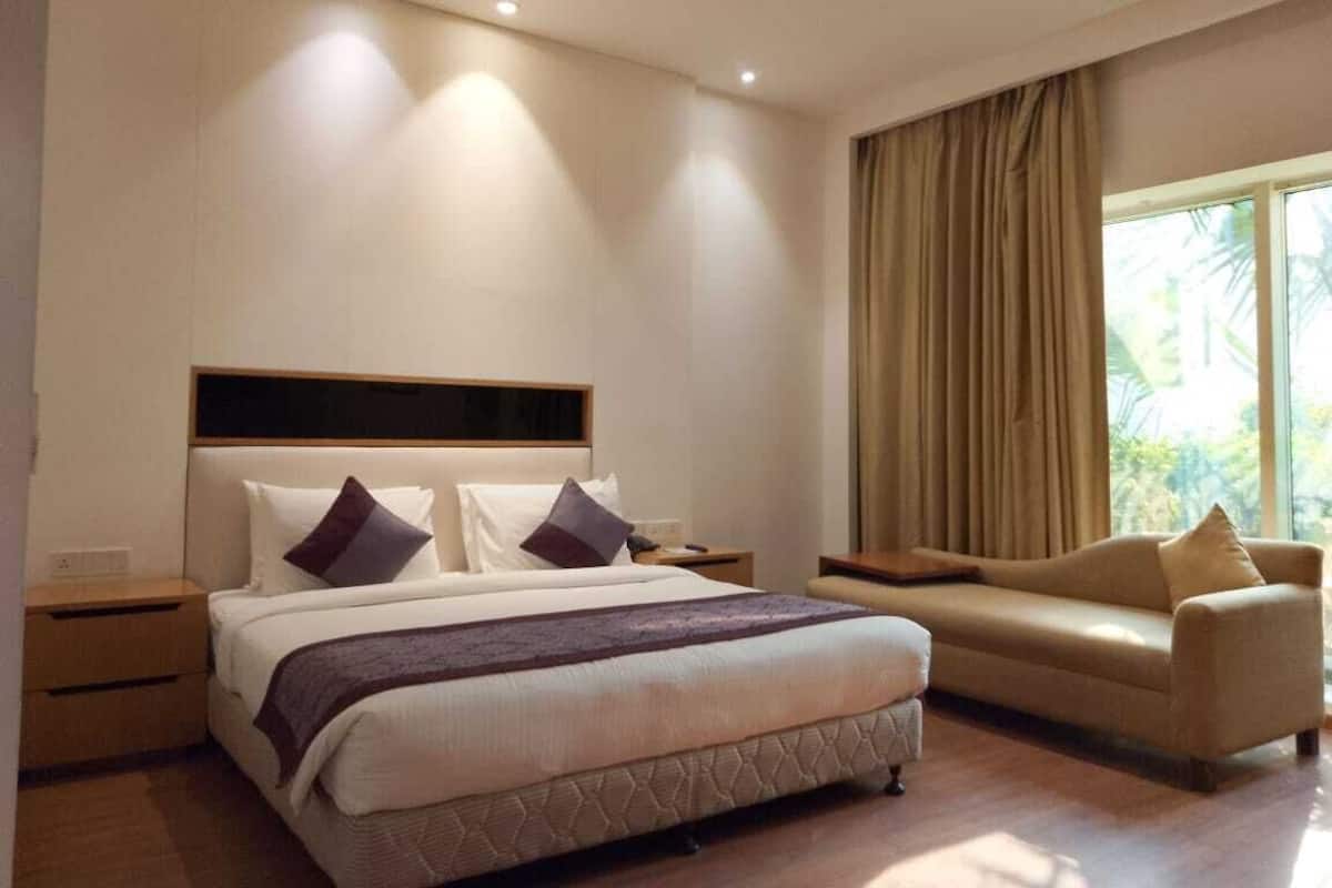 A modern hotel room with a large bed, a sofa, a nightstand, and a window with curtains.