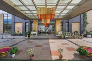A hotel entrance with a modern design, featuring a glass canopy and a decorative hanging element. - The Nikunj Hotels (New Delhi)