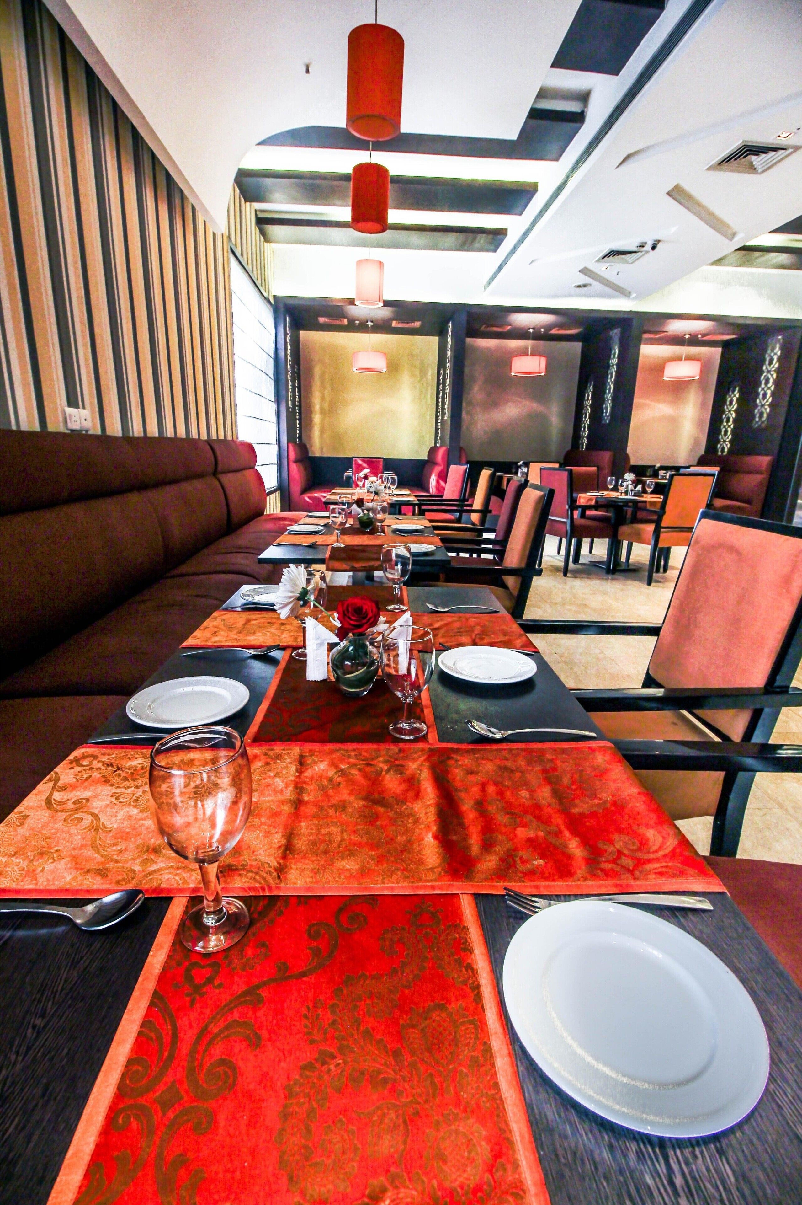 Ein Restaurant mit einem langen Esstisch, der für eine Mahlzeit gedeckt ist, mit rotem Tischläufer, weißen Tellern und einer Vase mit einer Rose.
