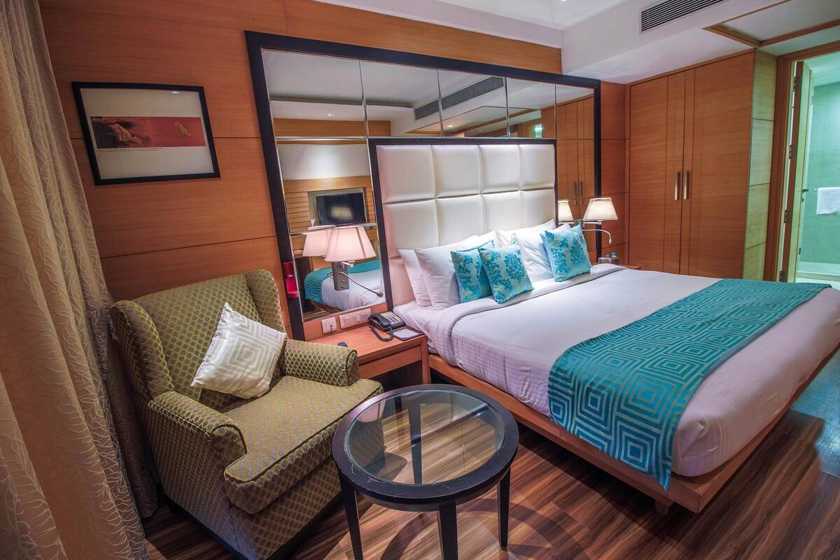 A hotel room with a bed, a sofa, a small table, a mirror, and a television.