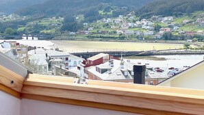 A balcony with a glass table, overlooking a town with a bridge and hills in the background. - The Cliffs - ViveMare (Viveiro)