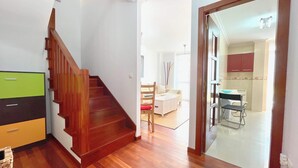 A staircase leading to a living area with a sofa, a dining table, and a kitchen area visible through an open door. - The Cliffs - ViveMare (Viveiro)