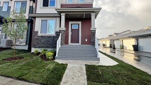 A two-story residential building with a front porch, a driveway, and a well-maintained lawn. - Elegant Escape w/King Bed|Long Stays|WEM|Disney+ (Edmonton)