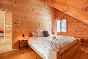 Un dormitorio acogedor tipo cabaña de madera con cama, almohadas, mesita de noche y ventana.