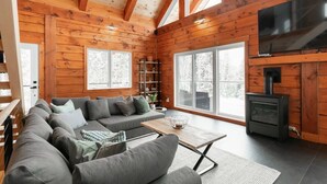 Ein gemütliches Blockhaus-Interieur mit Holzausbau, einer Sofagarnitur, einem Fernseher und einem Kamin.
