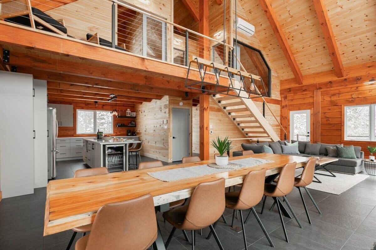 Une cabane en bois spacieuse comprenant un coin repas, une cuisine et un escalier reliant les deux niveaux.