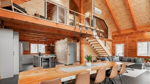 Eine geräumige Holzhütte mit Essbereich, Küche und einer Treppe, die zwei Ebenen verbindet.