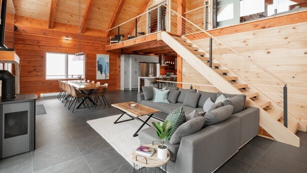 Ein großzügiger Wohnbereich mit Holzboden, einem grauen Sofa, einem Esstisch und einer Treppe.