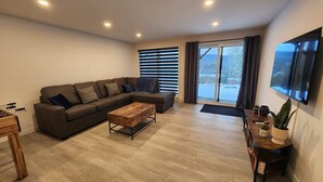 Un salon moderne avec un canapé d’angle, une table basse en bois et un grand téléviseur à écran plat fixé au mur.