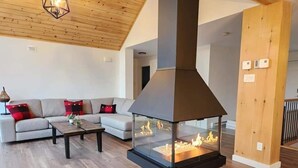 Un salon moderne doté d’une grande cheminée, d’un plafond en bois et d’un canapé agrémenté de coussins rouges.