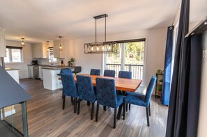 A modern kitchen with white cabinets, a wooden dining table with blue upholstered chairs, and a pendant light fixture.
