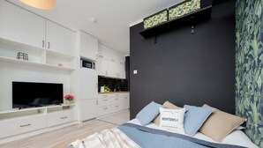 A modern bedroom with a bed, a TV, and a kitchenette. - Comfortable Studio with Balcony | Close to Metro and Park (Warszawa)