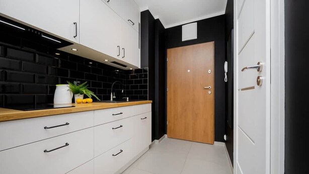 A modern kitchen with white cabinets, black backsplash, and a wooden countertop. - Comfortable Studio with Balcony | Close to Metro and Park (Warszawa)