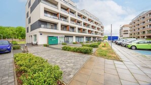 A multi-story hotel with a modern design, featuring balconies, a parking area, and a landscaped courtyard. - Comfortable Studio with Balcony | Close to Metro and Park (Warszawa)