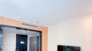 A modern living room with a flat-screen TV mounted on the wall, a wooden floor, and a door leading to another room. - Morning Wind Urban Hotel （May Fourth Square Branch) (Qingdao)