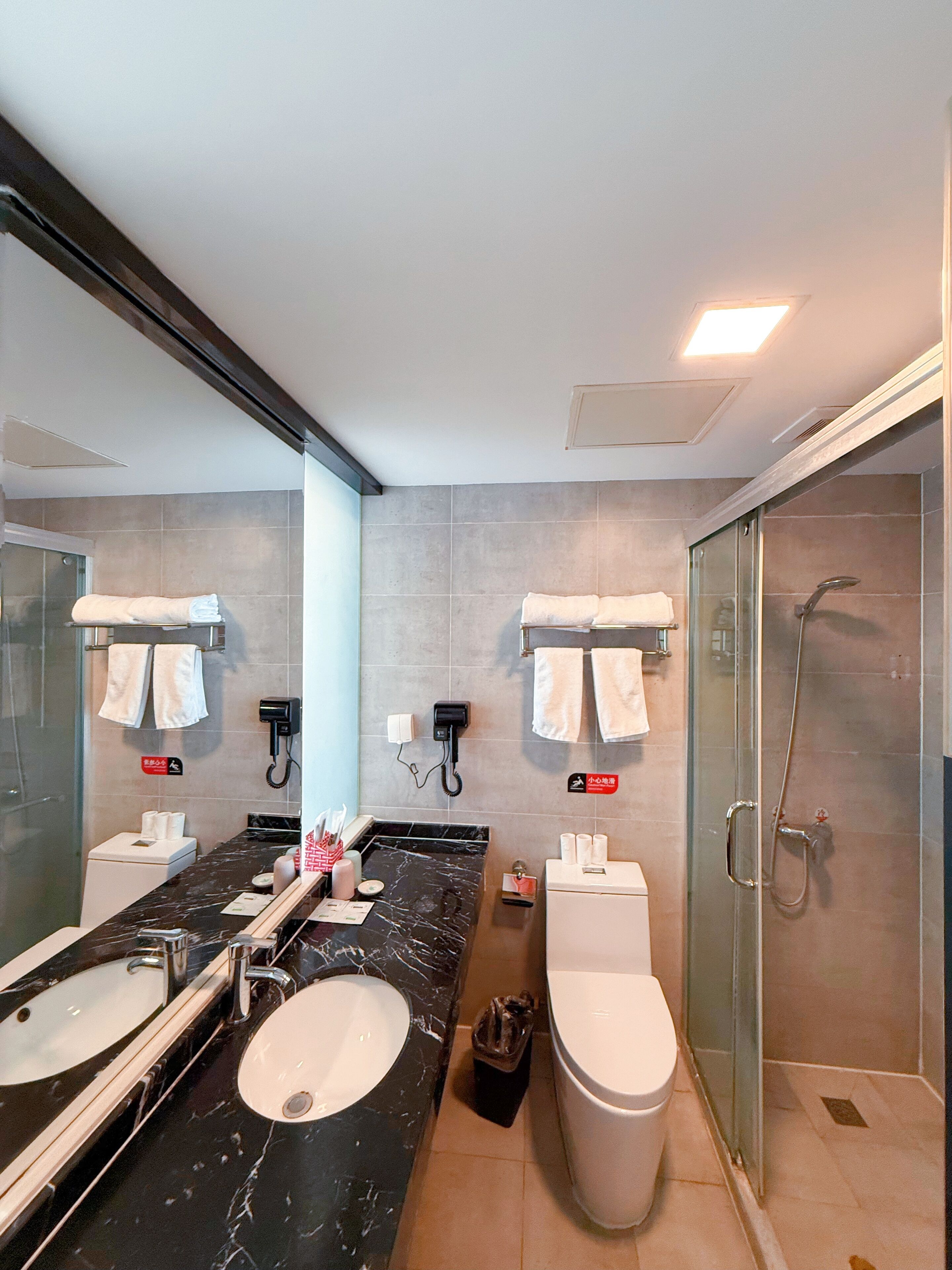 A modern bathroom with a large mirror, two sinks, a toilet, and a glass shower enclosure.