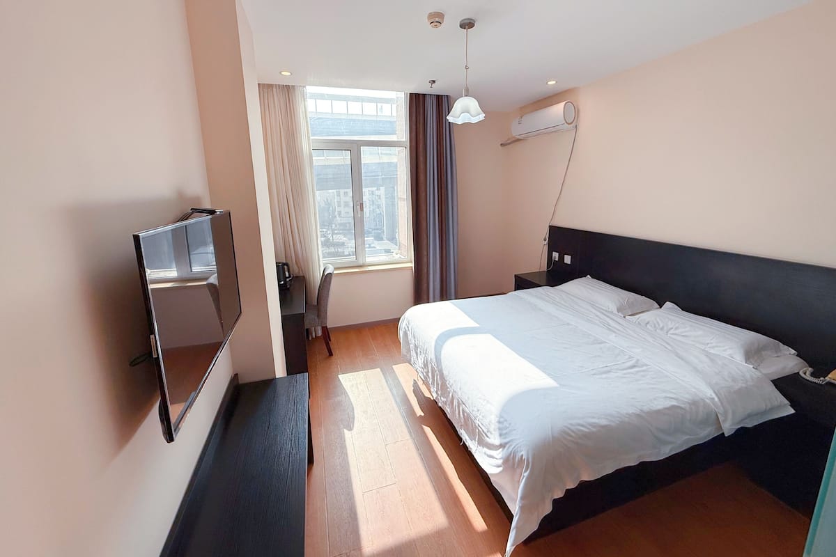 Ein Hotelzimmer mit einem Bett, einem Schreibtisch mit Stuhl, einem Fernseher und einem Fenster mit Vorhängen.