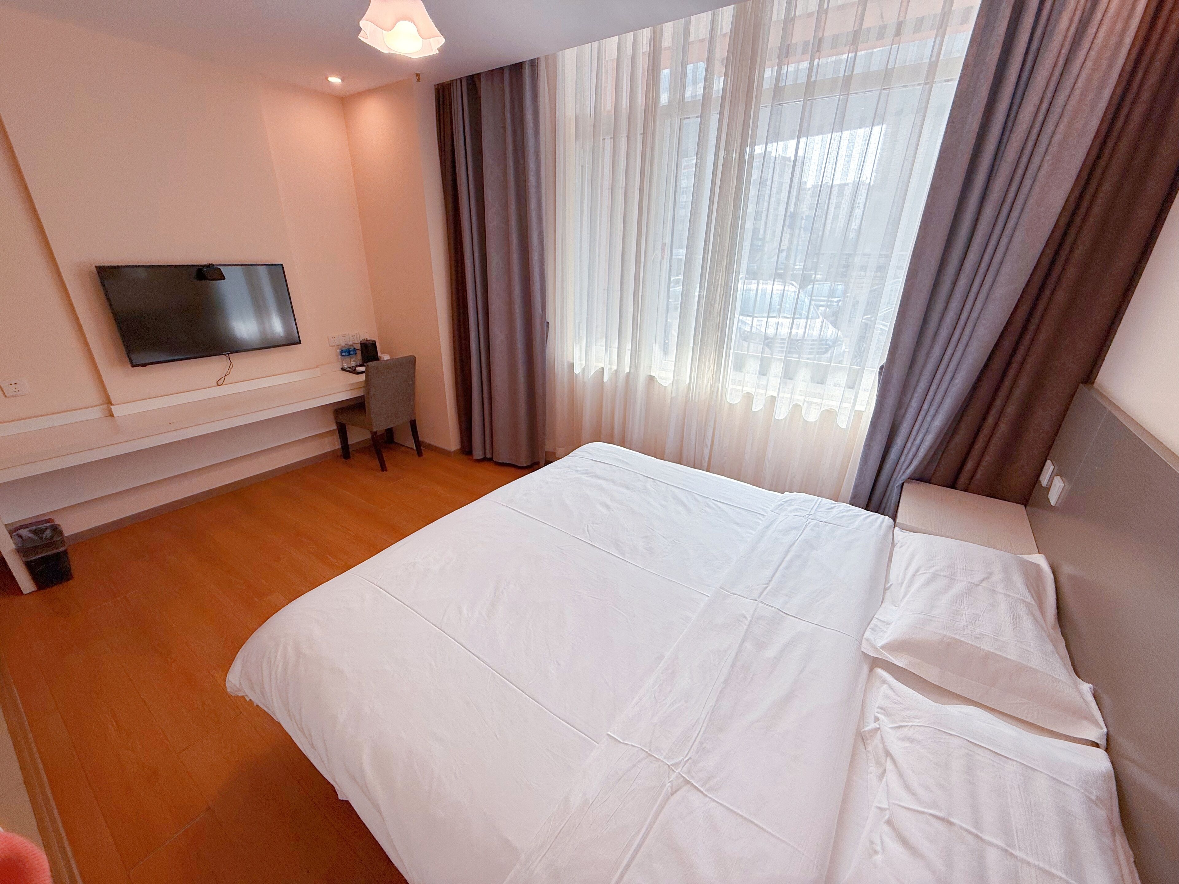 Una habitación de hotel con una cama grande, un escritorio, una silla, un televisor y una ventana con cortinas.