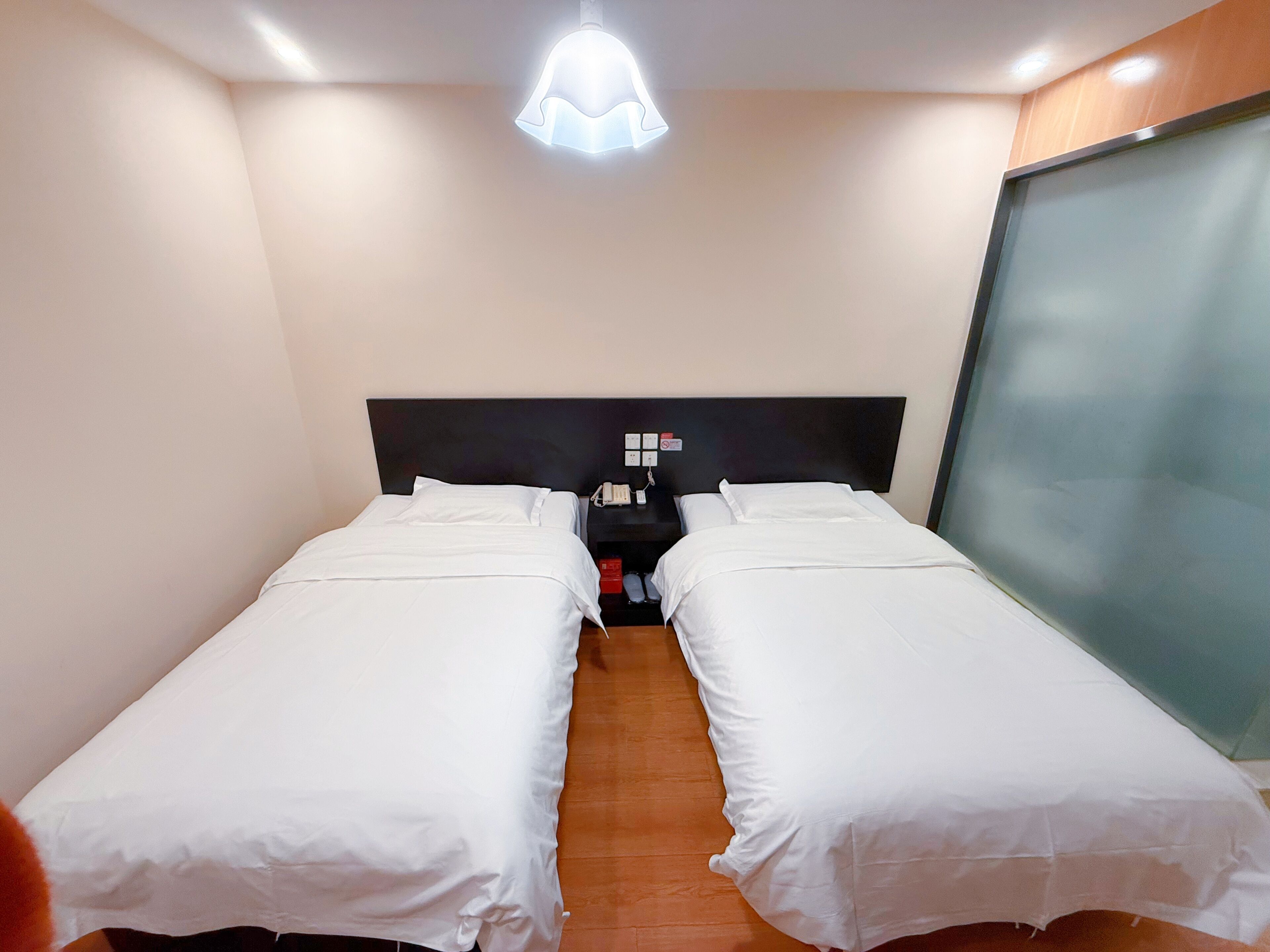 A hotel room with two single beds, a bedside table with a phone, and a modern light fixture.